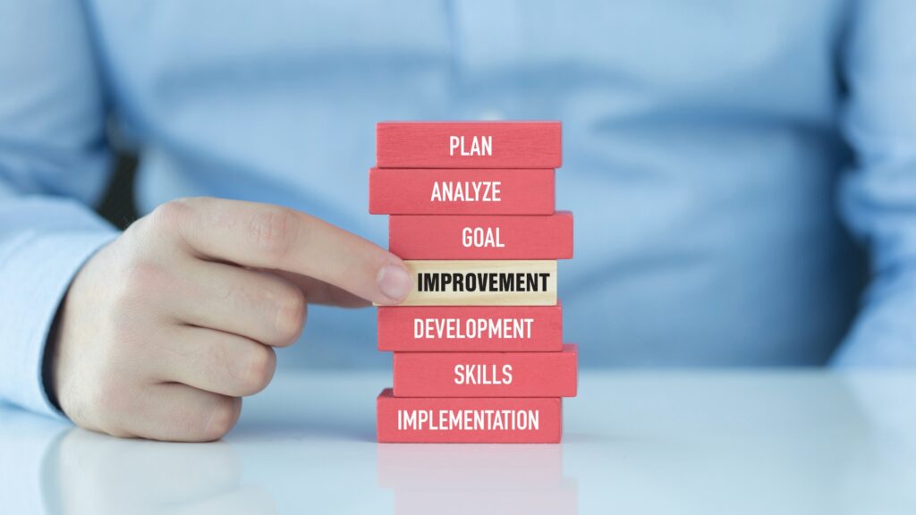 Üzletember kézzel egy fejlődést jelképező Jenga-szerű blokktornyot épít, amelyen a tervezés, elemzés, célok és fejlesztés lépései szerepelnek.